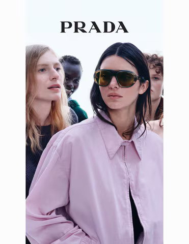 Das Bild zeigt eine Frau mit Sonnenbrille und fliederfarbenem Blouson. Im Hintergrund sind weitere Personen.