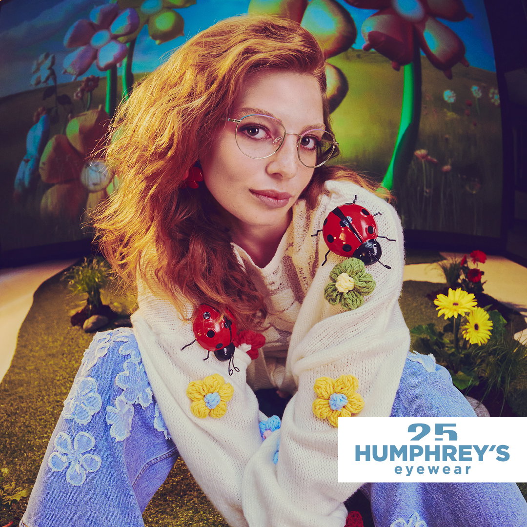 Das Bild zeigt eine junge Frau mit Brille mit vielen Blumen und Marienkäfern.
